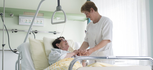 Pflegerin hält die Hand einer Patientin im Krankenbett