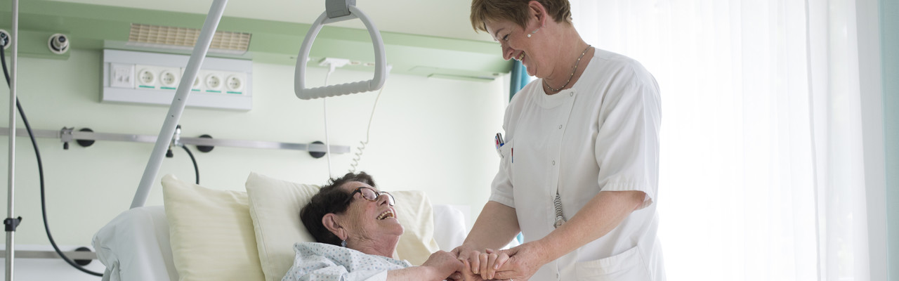 Eine Pflegerin hält die Hand einer Patienten in Ihrem Krankenbett